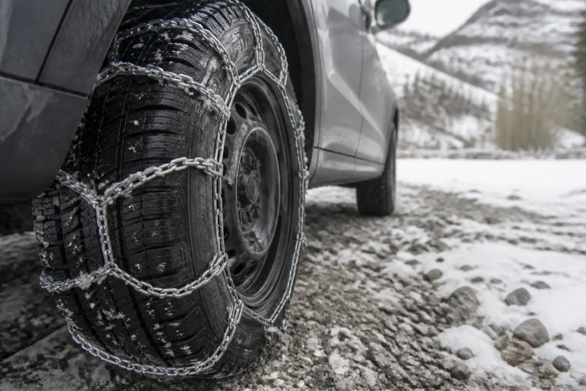 Chaînes à neige posées sur la roue d’une voiture au bord d’une route de montagne enneigée