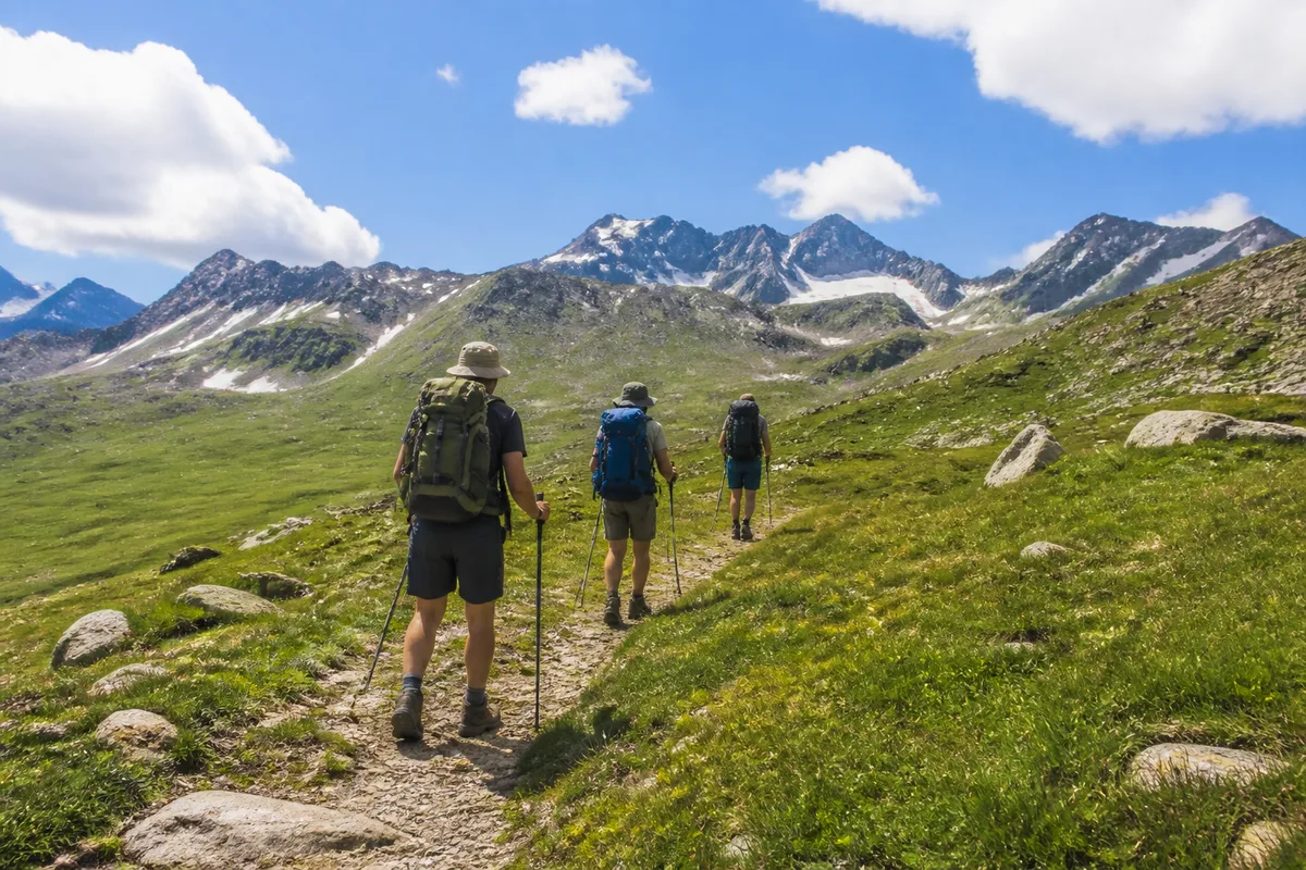 Randonneurs en file sur un sentier d’altitude, sac à dos et bâtons, ciel dégagé au-dessus des crêtes